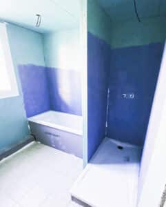 Salle de bain en rénovation avec baignoire JACKOBOARD et receveur de douche. Murs préparés, sol carrelé, plomberie installée.