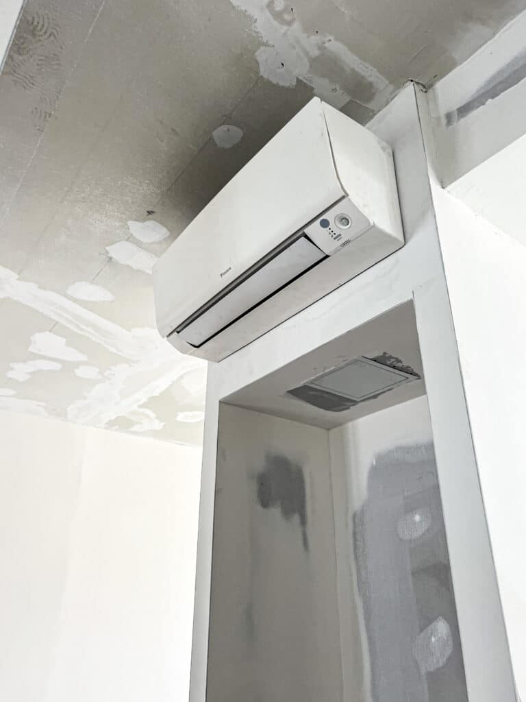 Climatiseur Daikin blanc fixé au mur d'une pièce en rénovation. Le plafond brut et les murs enduits indiquent un chantier.