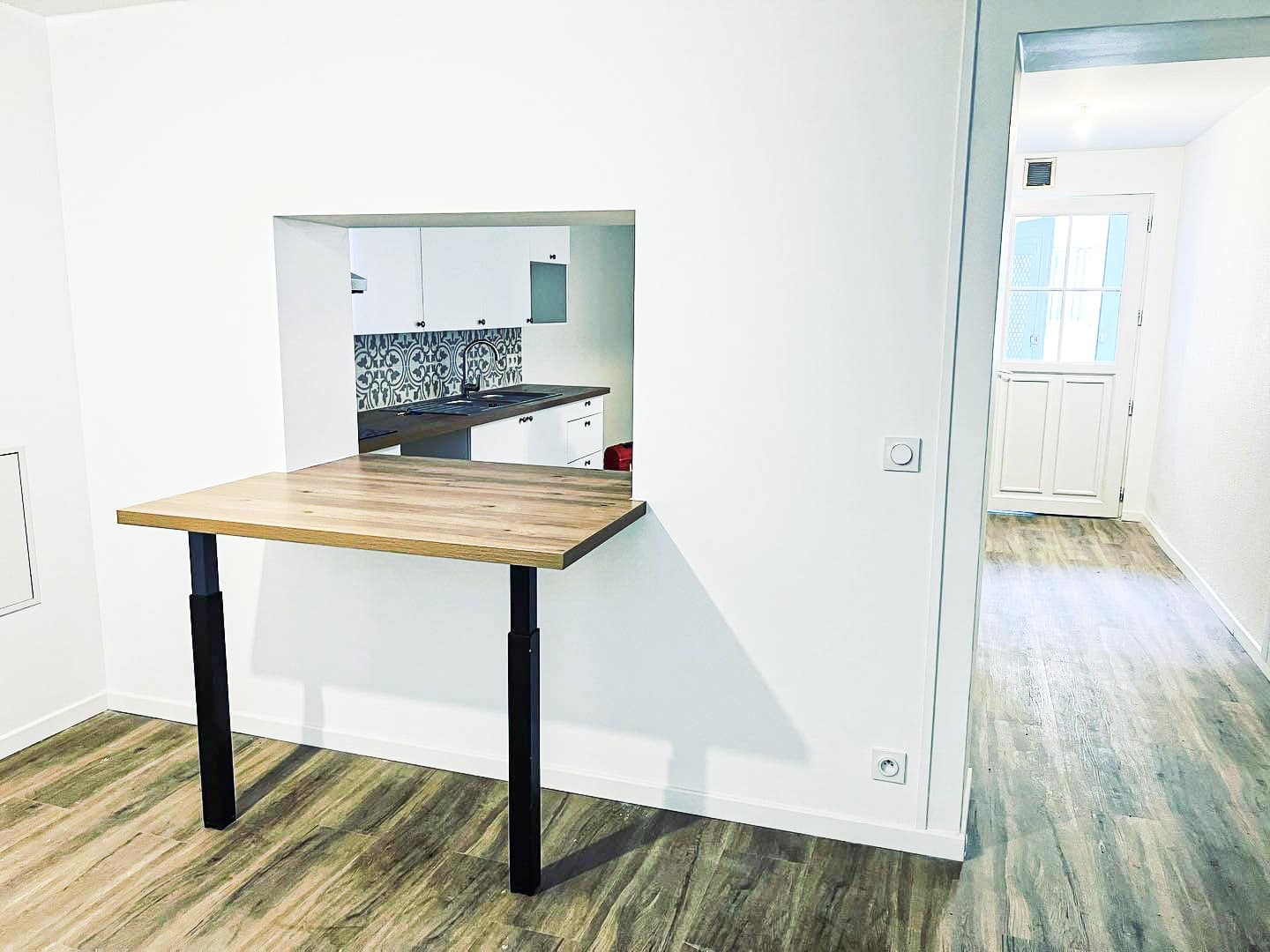 Cuisine moderne ouverte avec passe-plat et comptoir rabattable en bois clair, sol en parquet. Design épuré et fonctionnel.