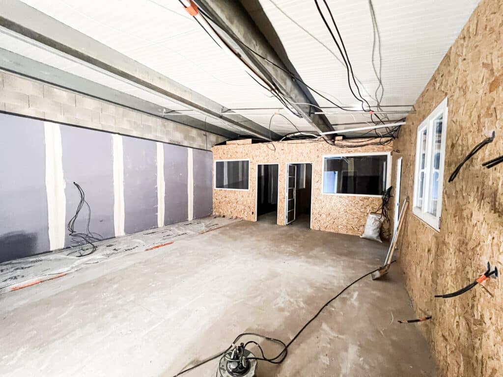 Pièce en cours de rénovation pour bureaux. Murs en placo et cloisons en OSB avec portes et fenêtres. Plafond exposé avec câbles, sol béton, pompe.