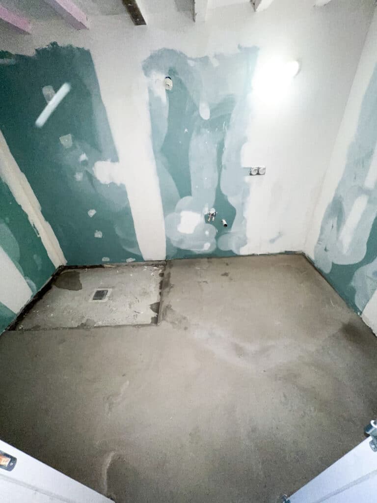 Salle de bain en rénovation avec murs Placo hydrofuges verts, sol béton brut, siphon de douche, raccords plomberie.