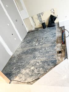 Chantier rénovation intérieure : plancher bois sombre, murs en plaques de plâtre jointées et murs dénudés. Tuyaux apparents.