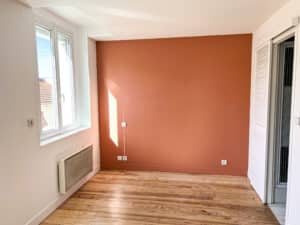 Pièce vide avec mur d'accent couleur terre cuite, plancher bois clair, fenêtre blanche et volet coulissant.