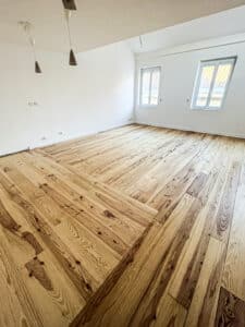 Chambre en rénovation avec plancher neuf en bois clair posé en chevrons et murs blancs, suspensions pendantes et fenêtres.