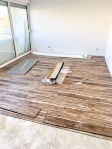 Pose de revêtement de sol vinyle imitation bois dans une pièce avec une porte coulissante vitrée, traces de pas visibles.