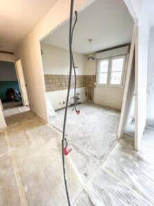 Rénovation de cuisine : démolition du sol et des meubles, tuyaux et conduits électriques apparents dans une pièce vide.