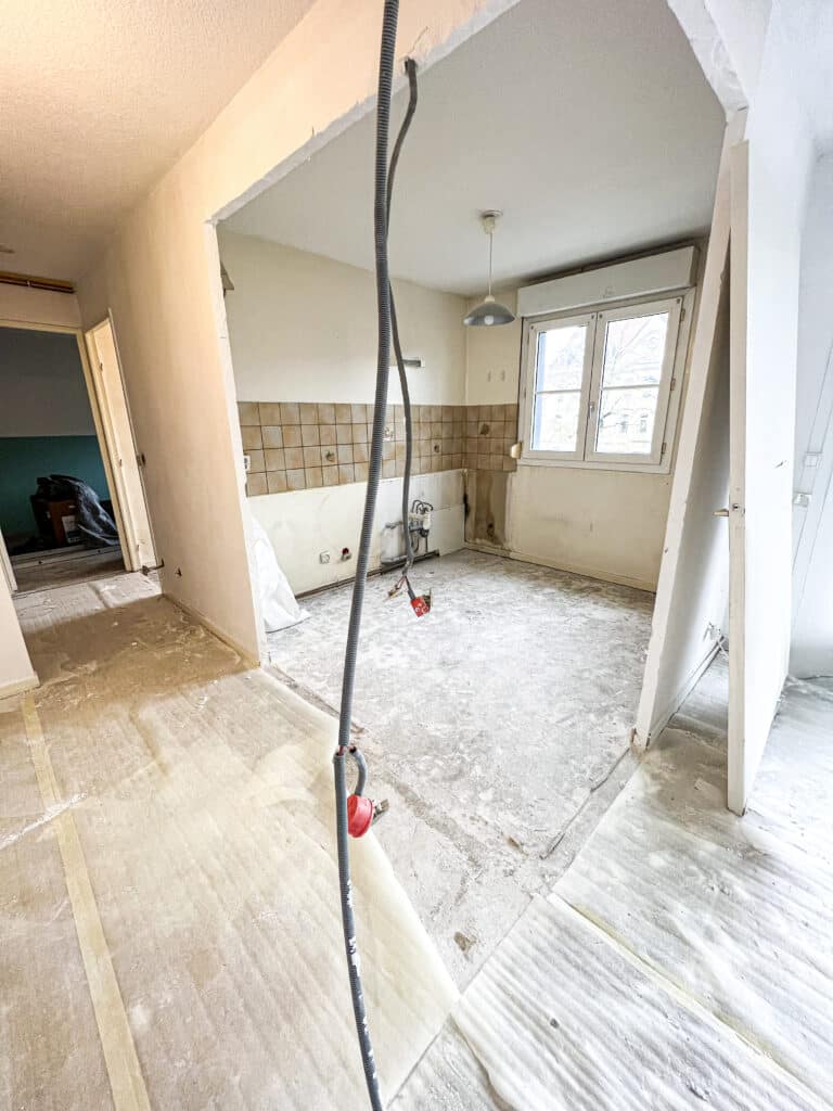 Rénovation Cuisine : Sol Nu, Démolition et Travaux Rénovation de cuisine : démolition du sol et des meubles, tuyaux et conduits électriques apparents dans une pièce vide.