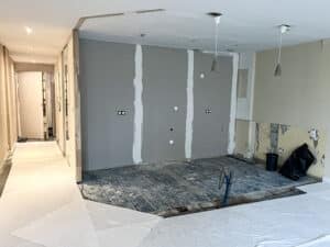 Chantier intérieur : murs en plaques de plâtre avec joints lissés, sol en lames de bois apparentes et zones protégées par un revêtement blanc.