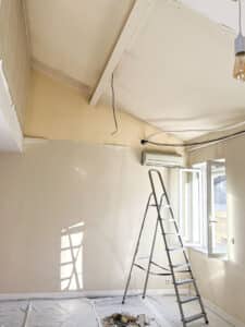 Rénovation intérieure d'une pièce mansardée avec échelle, fils électriques apparents et débris de travaux au sol.