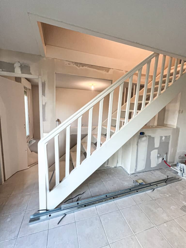Escalier en travaux de rénovation, balustrade blanche, murs en placo avec joints apparents, profil métallique "SPP CONTANT M48 34-36 500" au sol.