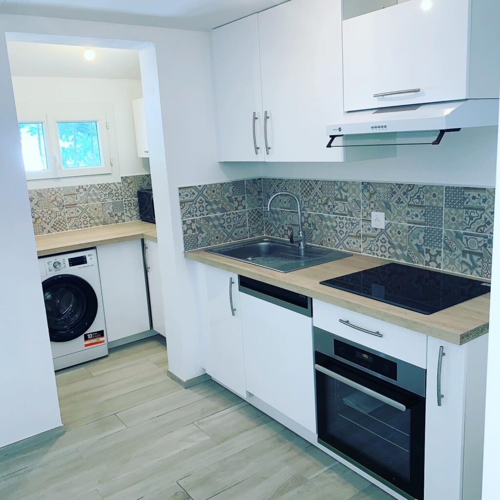 Aménagement petite cuisine moderne blanche et bois Cuisine moderne blanche avec plan de travail en bois, crédence graphique, évier et four encastré dans un petit espace.